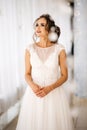 Beautiful bride in white wedding dress is standing in boudoir room and look up