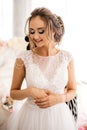 Beautiful bride in white wedding dress is standing in boudoir room and smiling