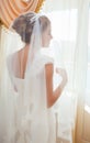 Bride in white wedding dress standing near the window