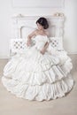 Beautiful bride woman sitting on luxuriant wedding dress over white modern interior Royalty Free Stock Photo