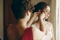 Beautiful bridesmaid helping brunette bride in white wedding dress put on luxury earrings, morning wedding preparation, bride with Royalty Free Stock Photo