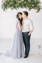 Beautiful bridesmaid in pine wreath with handsome groomsman in the studio hugging.