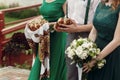 Beautiful bridesmaids in stylish green dress with white flowers bouquet and holding traditional bread with handsome groomsman at