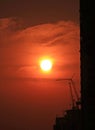 Beautiful bright setting sun on deep orange color sky over the silhouette of construction site in Bangkok, Thailand Royalty Free Stock Photo