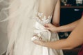 Beautiful brunette bride putting on wedding dress, bridesmaids helping bride tie wedding corset close-up in hotel room, Royalty Free Stock Photo