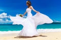 Beautiful brunette bride in white wedding dress with big long white train and with wedding bouquet stand on shore sea. Tropical s Royalty Free Stock Photo