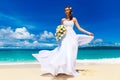 Beautiful brunette bride in white wedding dress with big long white train and with wedding bouquet stand on shore sea. Tropical s Royalty Free Stock Photo