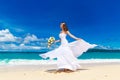 Beautiful brunette bride in white wedding dress with big long white train and with wedding bouquet stand on shore sea. Tropical s Royalty Free Stock Photo