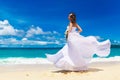 Beautiful brunette bride in white wedding dress with big long white train and with wedding bouquet stand on shore sea. Tropical s Royalty Free Stock Photo