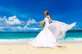 Beautiful brunette bride in white wedding dress with big long white train and with wedding bouquet stand on shore sea. Tropical s Royalty Free Stock Photo