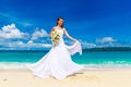 Beautiful brunette bride in white wedding dress with big long white train and with wedding bouquet stand on shore sea. Tropical s Royalty Free Stock Photo