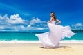 Beautiful brunette bride in white wedding dress with big long white train and with wedding bouquet stand on shore sea. Tropical s Royalty Free Stock Photo