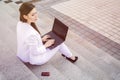 Beautiful brunette business woman in white suit with notebook on her lap, typing, working outdoors. Copy space Royalty Free Stock Photo