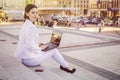 Beautiful brunette business woman in white suit with notebook on her lap, typing, working outdoors. Copy space Royalty Free Stock Photo