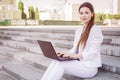 Beautiful brunette business woman in white suit with notebook on her lap, typing, working outdoors. Copy space Royalty Free Stock Photo