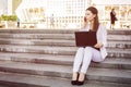 Beautiful brunette business woman in white suit with notebook on her lap, typing, working outdoors. Copy space Royalty Free Stock Photo