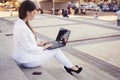 Beautiful brunette business woman in white suit with notebook on her lap, typing, working outdoors Royalty Free Stock Photo