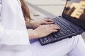 Beautiful brunette business woman in white suit with notebook on her lap, typing, working outdoors. Hands on a keyboard close up Royalty Free Stock Photo