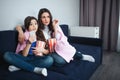 Beautiful brunette caucasian mother and daughter sit together in room. Scared adult and small women watch movie and eat Royalty Free Stock Photo