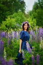 A beautiful brunette is dancing in a blue dress in a field among lupines. Portrait on a meadow with lilac-pink flowers Royalty Free Stock Photo