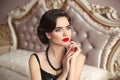 Beautiful brunette, elegant woman portrait. Manicure nails. Retro lady with red lips makeup, wavy hairstyle posing on modern bed Royalty Free Stock Photo