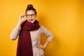 A beautiful brunette with gathered hair in a burgundy scarf looks with astonishment to the side, adjusting her glasses. Royalty Free Stock Photo