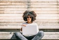 Beautiful brunette girl with afro hair sitting cross legged looks straight ahead while using a laptop Royalty Free Stock Photo