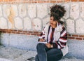 Beautiful brunette girl with afro hair writes in her diary relaxingly while sitting next to a large stone and brick wall Royalty Free Stock Photo