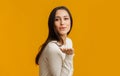 Beautiful brunette girl blowing kiss at camera, posing over yellow background Royalty Free Stock Photo