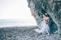 Beautiful brunette girl in blue dress, white flower in hair sitting near the cliff, the sea, viewing profile, Royalty Free Stock Photo