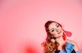 Beautiful brunette girl with blue makeup, pigtails and a sleeveless denim vest posing on a red background with a heart-shaped