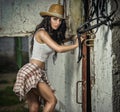 Beautiful brunette girl with country look, indoors shot in stable, rustic style. Attractive woman with cowboy hat, denim shorts Royalty Free Stock Photo