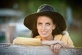 Beautiful brunette girl with country look near an old wooden fence. Attractive woman with black hat and yellow coat Royalty Free Stock Photo