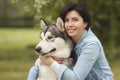 Beautiful brunette girl sitting on the grass with her funny friend malamute dog