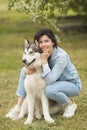 Beautiful brunette girl sitting on the grass with her funny friend malamute dog