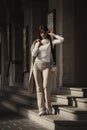 beautiful brunette girl dressed in white blouse, pants, sneakers with a handbag and camel coat in hands. Stylish trendy Royalty Free Stock Photo