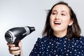 Beautiful brunette girl with eyes closed screaming singing into a Hairdryer on hand isolate the blue shirt happiness emotions the Royalty Free Stock Photo