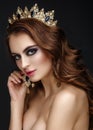 Beautiful brunette girl with a golden crown, earrings and professional evening make-up