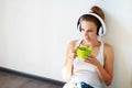 Beautiful brunette girl with headphones listening to music and drinking coffee while sitting on the floor in an empty room against Royalty Free Stock Photo