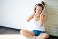 Beautiful brunette girl with headphones listening to music while sitting on the floor in an empty room on the white wall Royalty Free Stock Photo