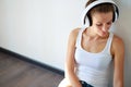 Beautiful brunette girl with headphones listening to music while sitting on the floor in an empty room on the white wall Royalty Free Stock Photo