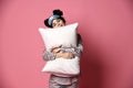 Beautiful brunette girl just woke up and hugging soft pillow. Woman yawning smiling sleepy day on pink Royalty Free Stock Photo