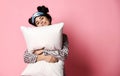 Beautiful brunette girl just woke up and hugging soft pillow. Woman yawning smiling sleepy day on pink Royalty Free Stock Photo