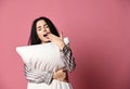 Beautiful brunette girl just woke up with soft pillow and feathers. Woman yawning sleepy day on pink Royalty Free Stock Photo