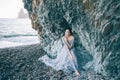 Beautiful brunette girl in a long grey dress with a veil sitting by the sea, near the cliff, Royalty Free Stock Photo