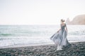 Beautiful brunette girl in long grey winding in the wind dress is made of tulle holds with one hand the dress looks profile