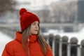 Beautiful brunette girl with long hair in red down jacket and knitted hat with bubo. Young woman in stylish winter clothes outside Royalty Free Stock Photo