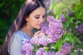 Beautiful brunette girl, with long hair, smells lilac flowers, in the summer in the park, sunny day