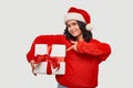 Beautiful brunette girl in a red sweater and Santa Claus hat holding white giftbox with red ribbon Royalty Free Stock Photo
