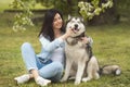 Beautiful brunette girl sitting on the grass with her funny friend malamute dog